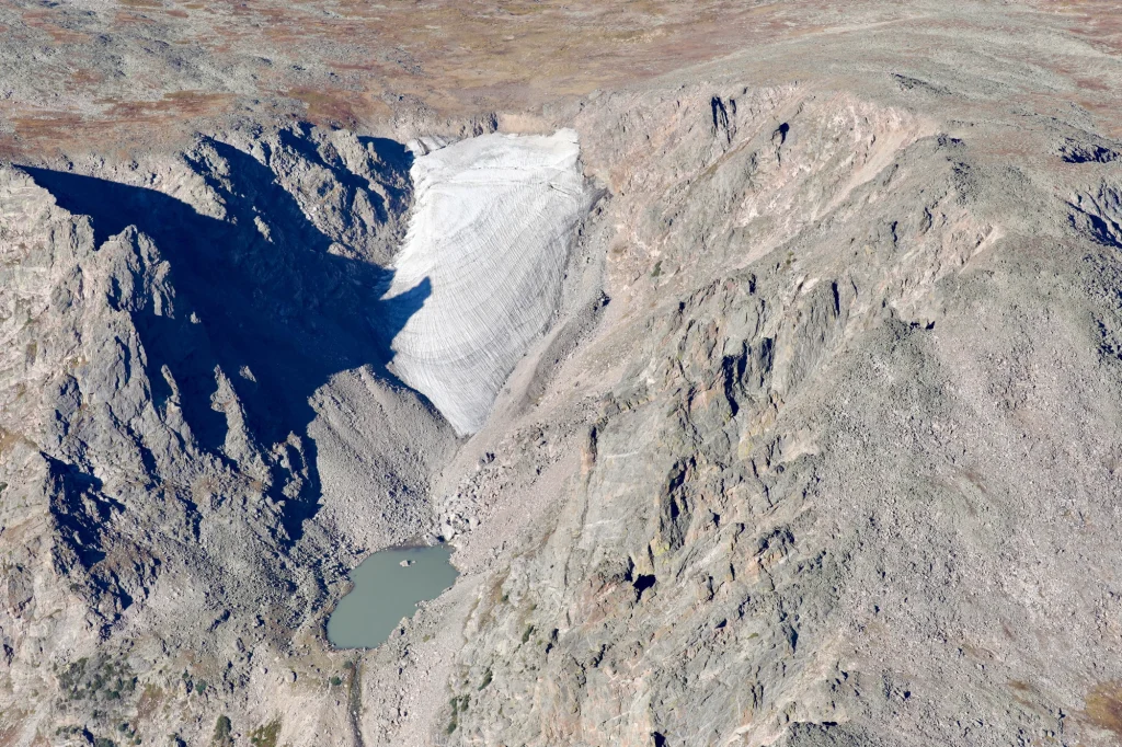 A glacier rests between two rock faces high on a mountain peak.