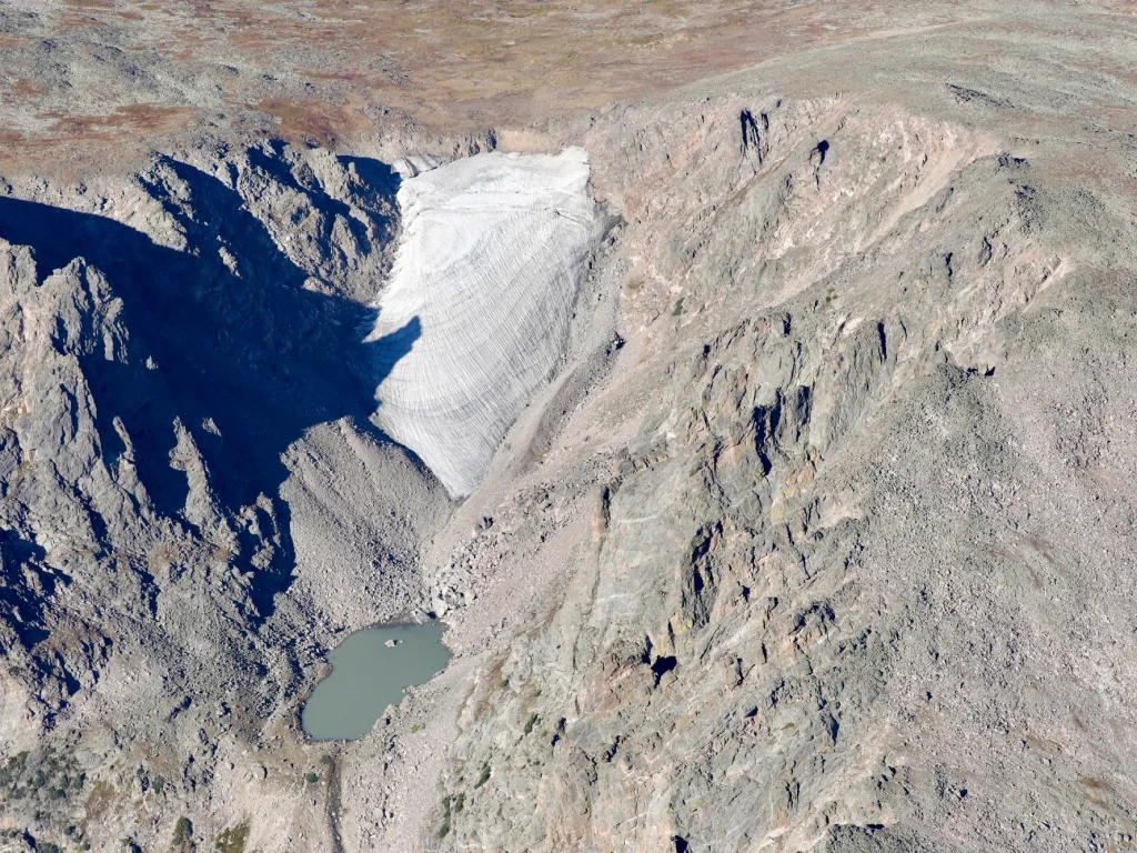A glacier rests between two rock faces high on a mountain peak.