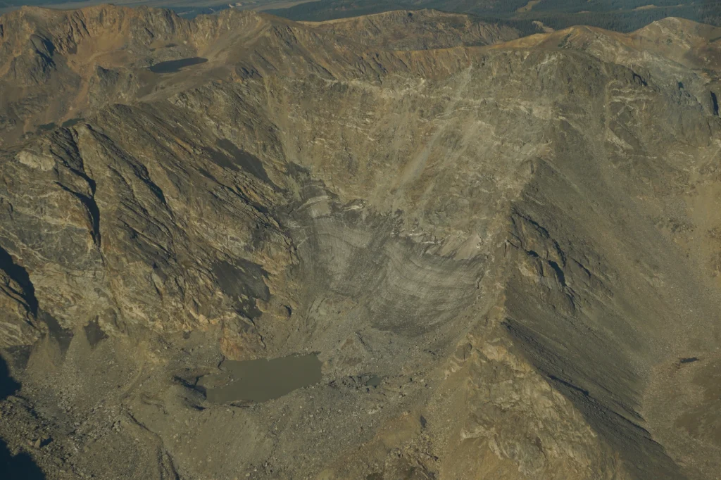 Ice from a glacier is barely visible thanks to dirt and rocks covering the ice, blending it into the rock face.